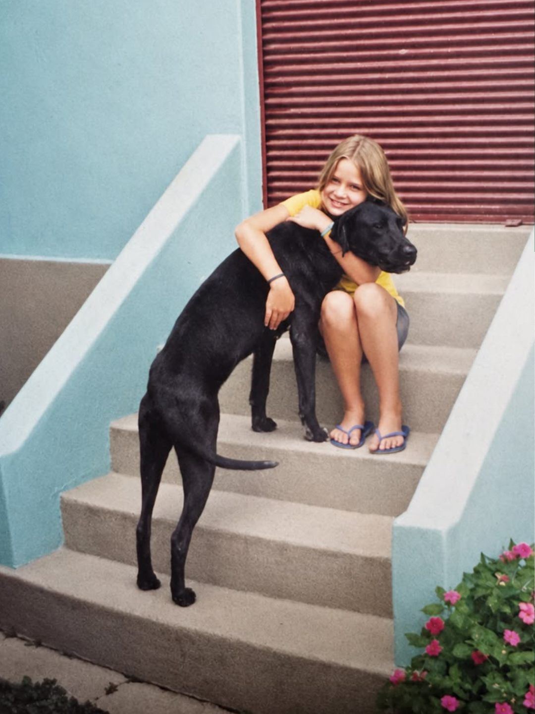 Bruna criança abraçando um cachorro preto na escada de casa