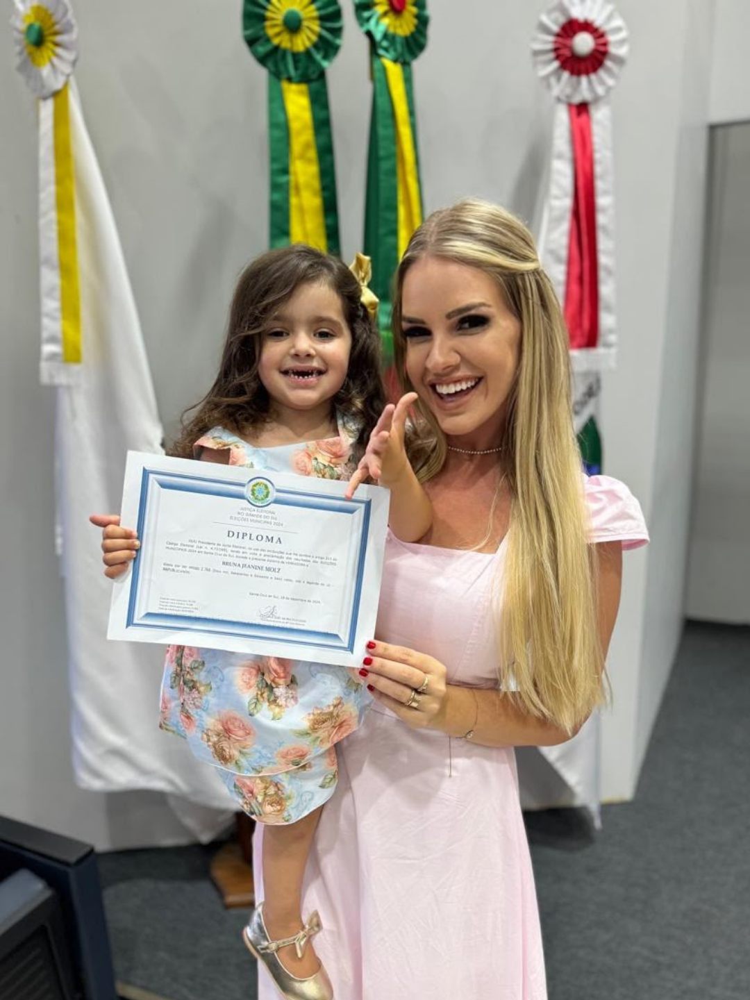 Bruna com a filha no colo segurando o diploma da Justiça Eleitoral, eleições 2024